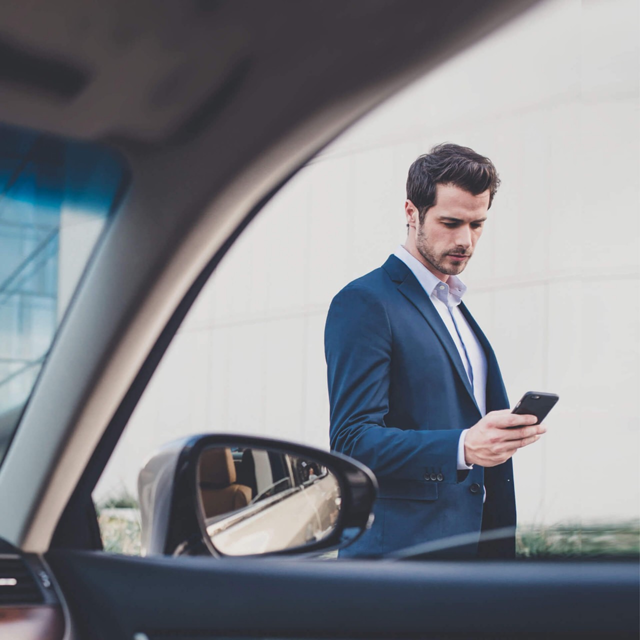 man looking at his phone next to a car